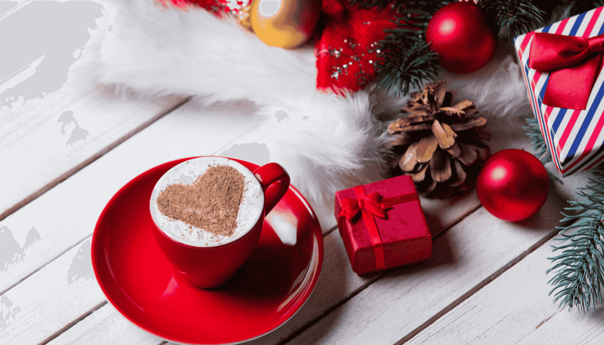 Red mug with heart-shaped cinnamon on a white wooden surface with Christmas decorations.