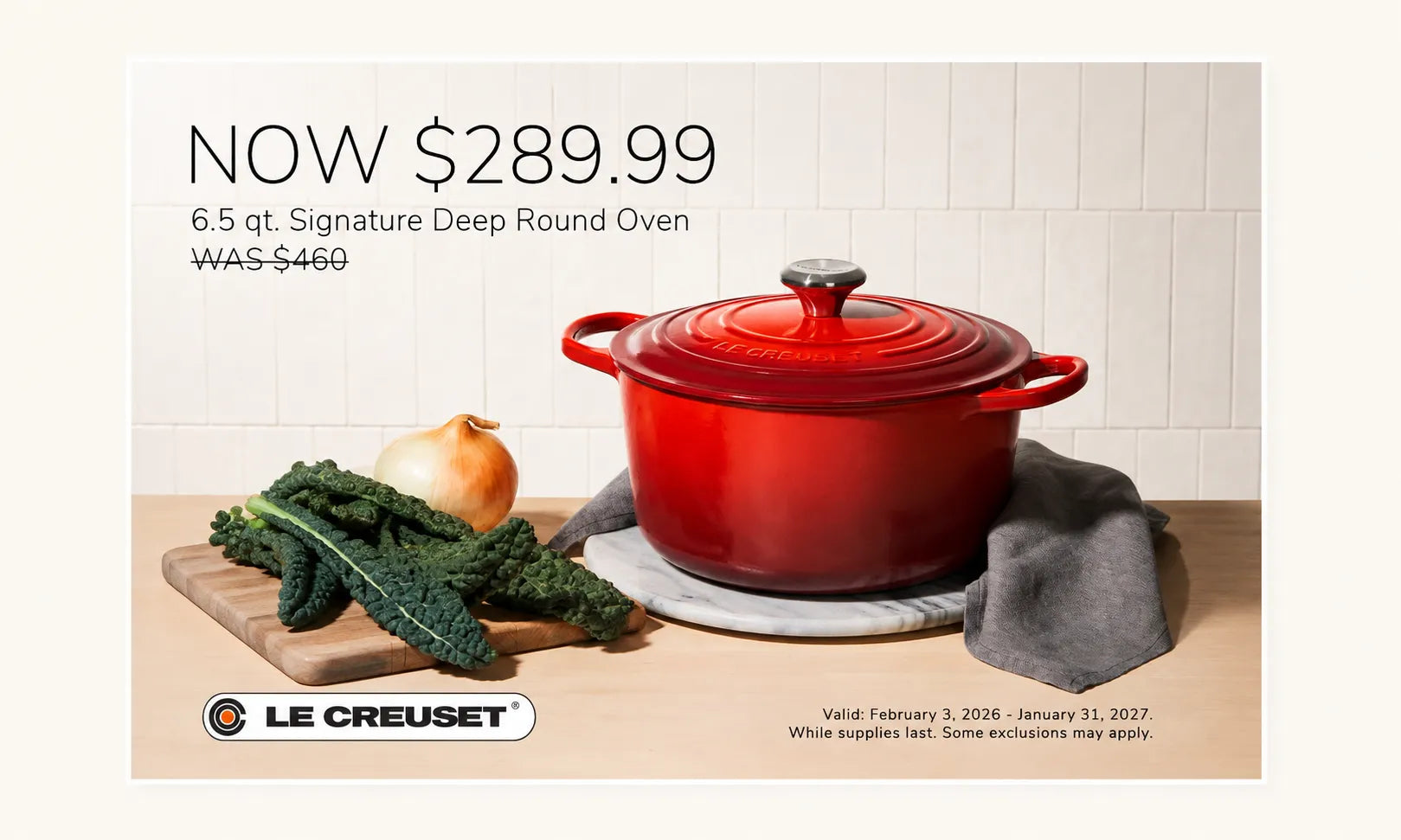 Le Creuset 6.5 qt Signature Deep Round Oven in red enamel, shown in a kitchen-style still life with kale, an onion, a cutting board, and a gray cloth.
