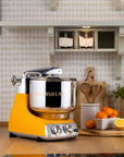 Yellow kitchen stand mixer on a countertop with a kitchen setting in the background