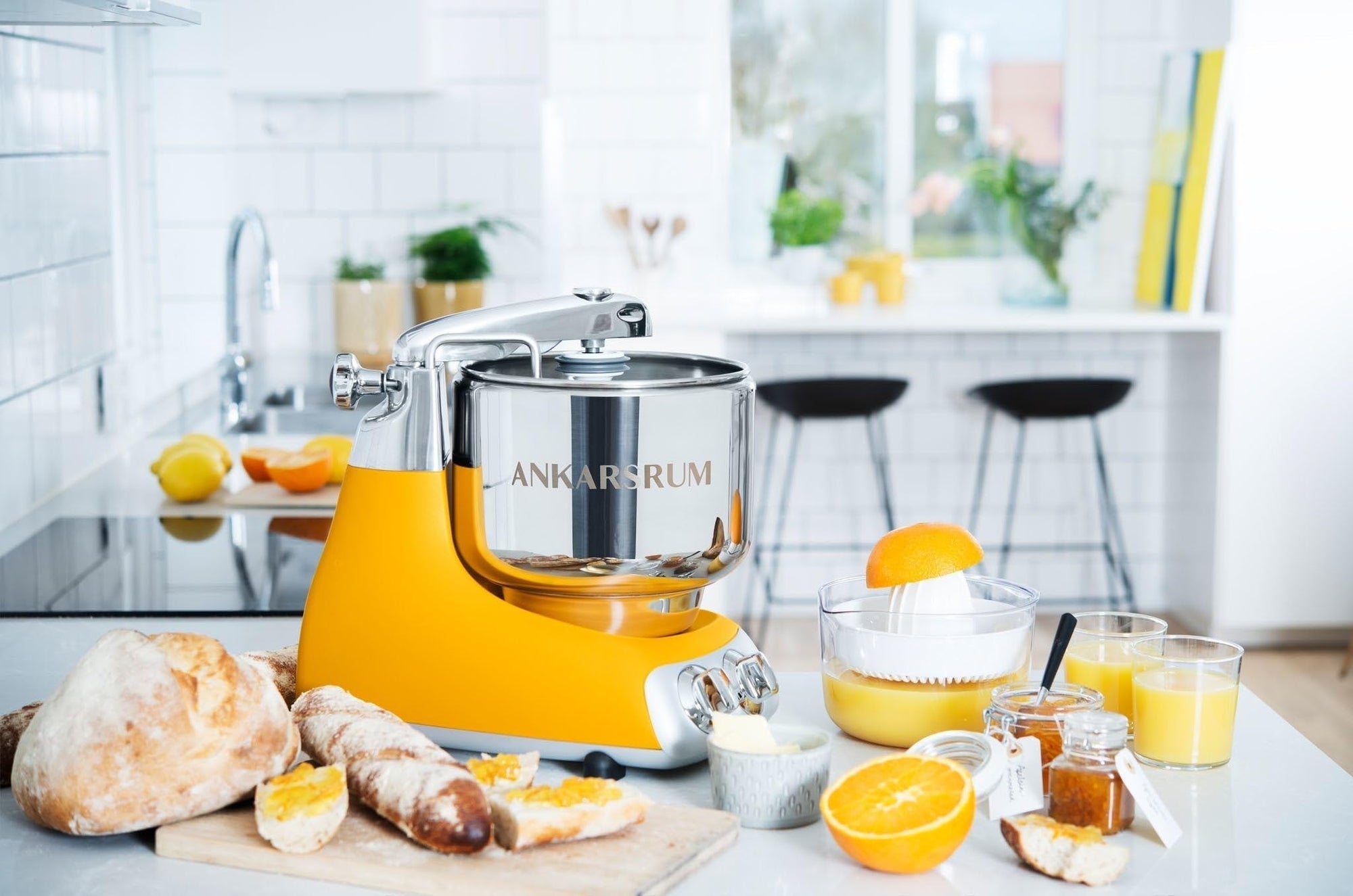 Yellow kitchen stand mixer with 'Ankarsrum' branding on a kitchen counter with food surrounding it
