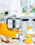Yellow kitchen stand mixer with 'Ankarsrum' branding on a kitchen counter with food surrounding it