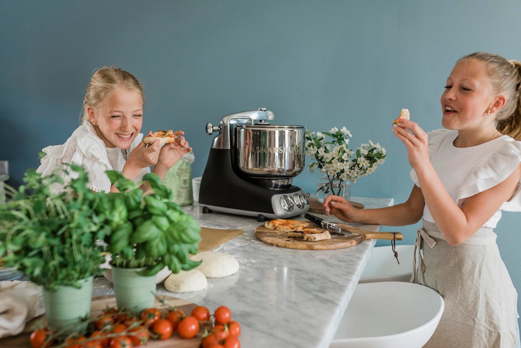 Two young girls in a kitchen preparing food with a stand mixer.