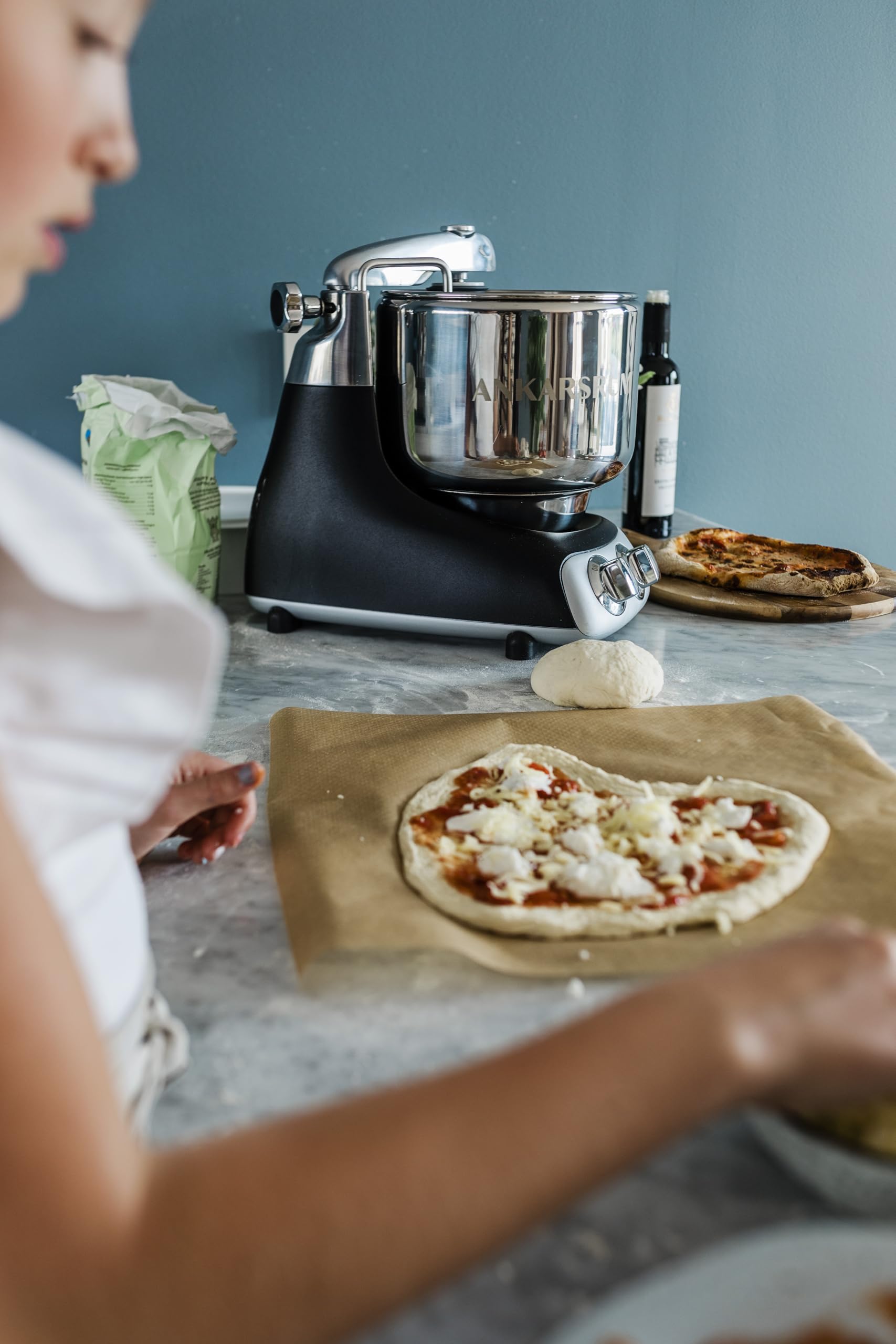 Person making a pizza with a black stand mixer in the background