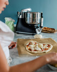 Person making a pizza with a black stand mixer in the background