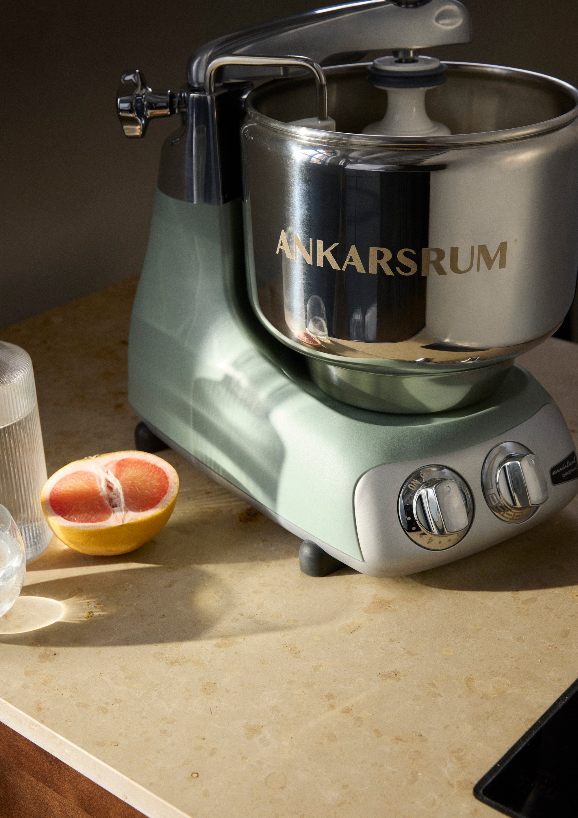 Ankarsrum nordic sage stand mixer on a countertop with a half-grapefruit and a glass of water.