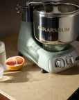 Ankarsrum nordic sage stand mixer on a countertop with a half-grapefruit and a glass of water.