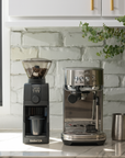 Coffee grinder and espresso machine on a kitchen counter with a white brick wall background.