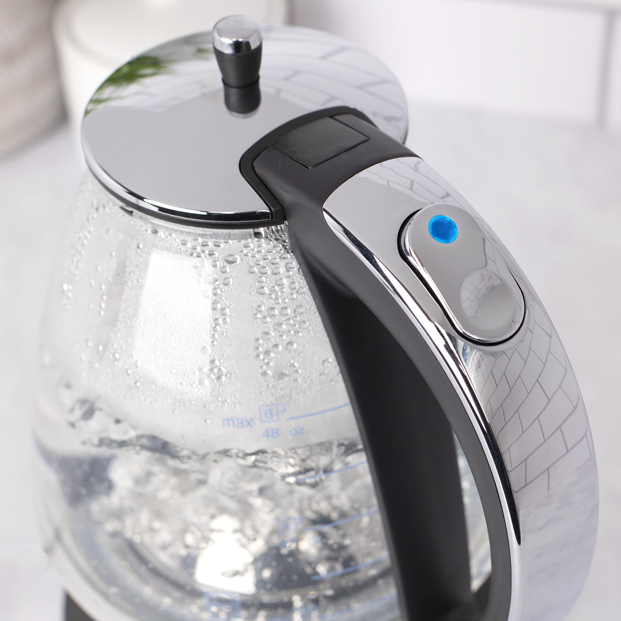 Close up of blue indicator button on a black and polished chrome Capresso 48 oz electric kettle displayed on a white background