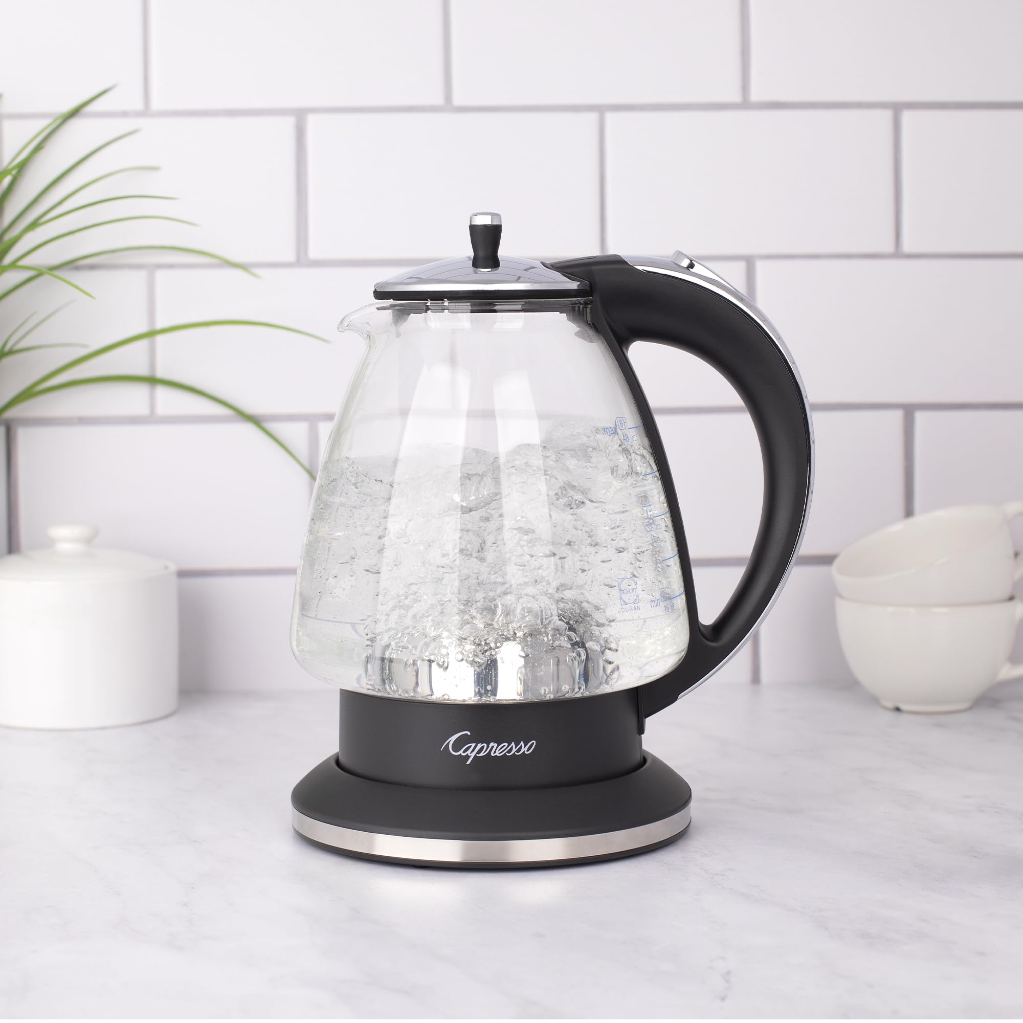 Black and polished chrome Capresso 48 oz electric kettle with water boiling on a kitchen counter