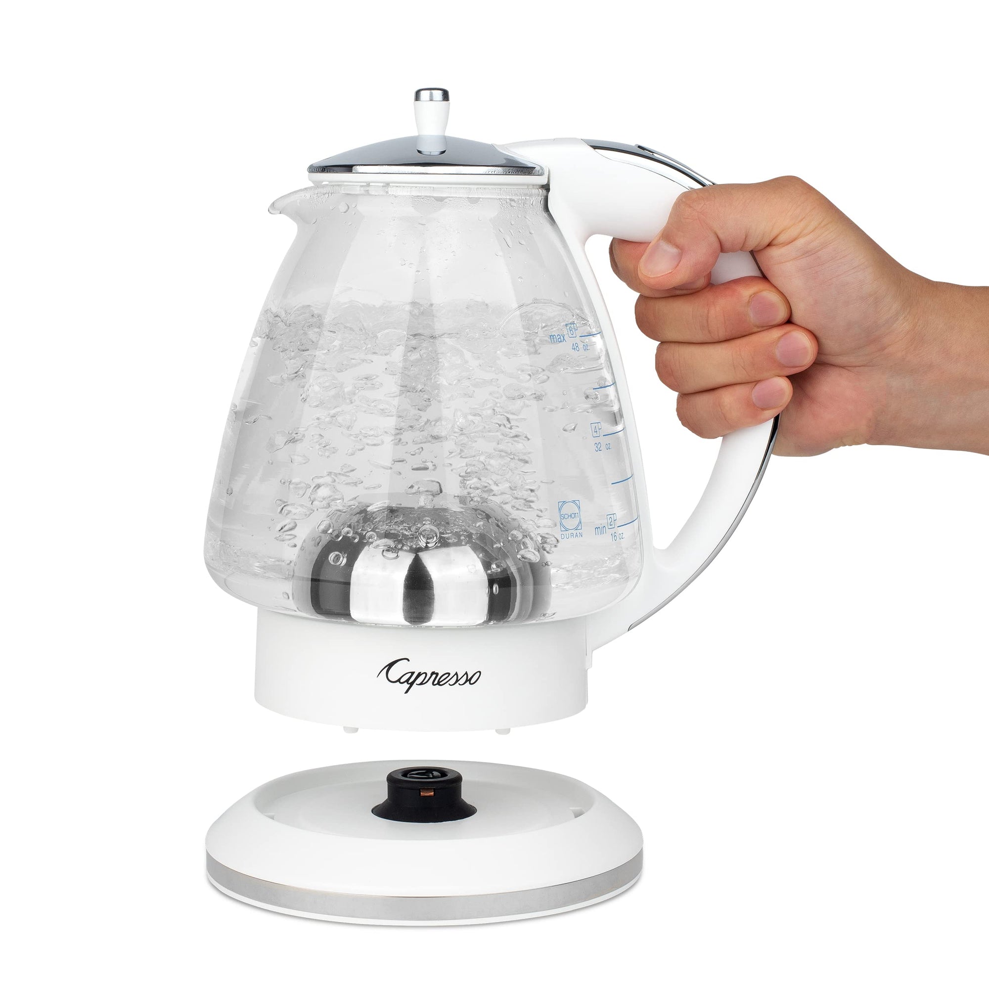 White and polished chrome Capresso 48 oz electric kettle with handle, held by a hand on a white background.
