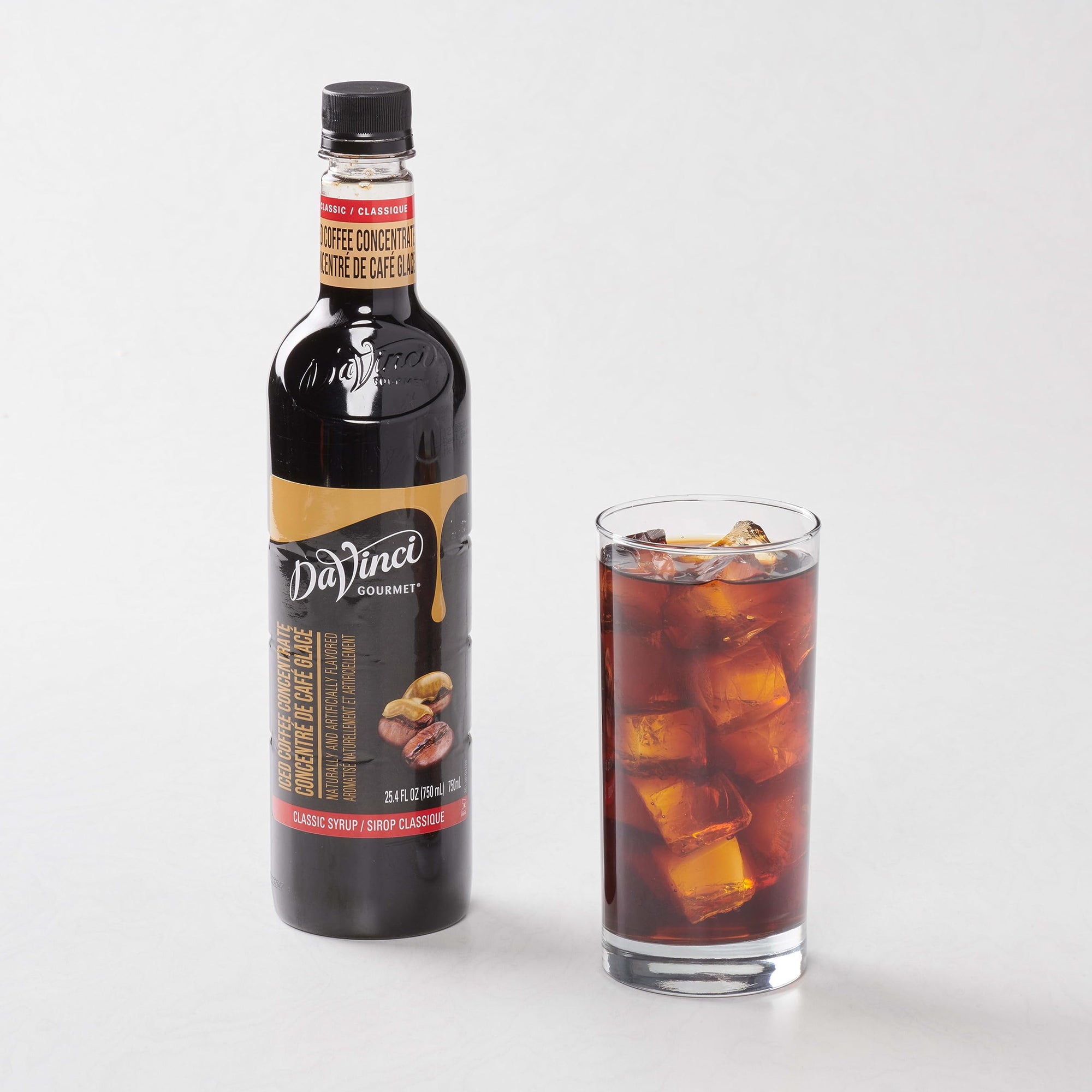 Bottle of DaVinci Gourmet syrup next to a glass of iced coffee on a white background