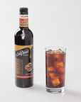 Bottle of DaVinci Gourmet syrup next to a glass of iced coffee on a white background