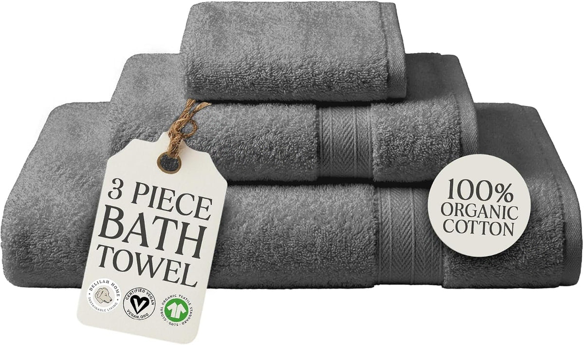 A 3-piece set of folded dark gray cotton bath towels with a hanging tag that reads '3 PIECE BATH TOWEL' and a circular badge that says '100% ORGANIC COTTON'.