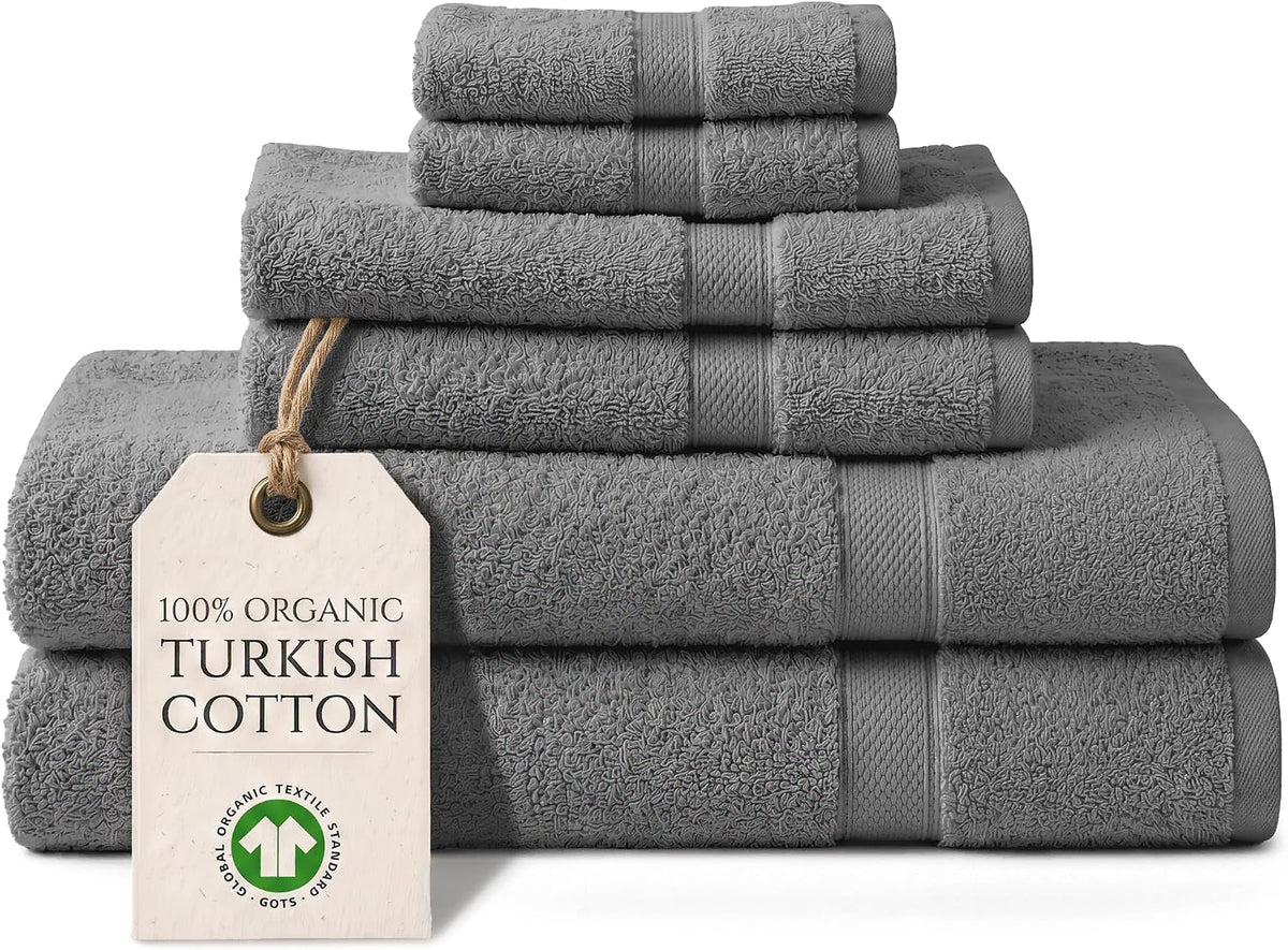 A stack of six dark gray cotton bath towels in various sizes, including hand towels, washcloths, and towels, with a paper tag that reads '100% ORGANIC TURKISH COTTON' on a white background.