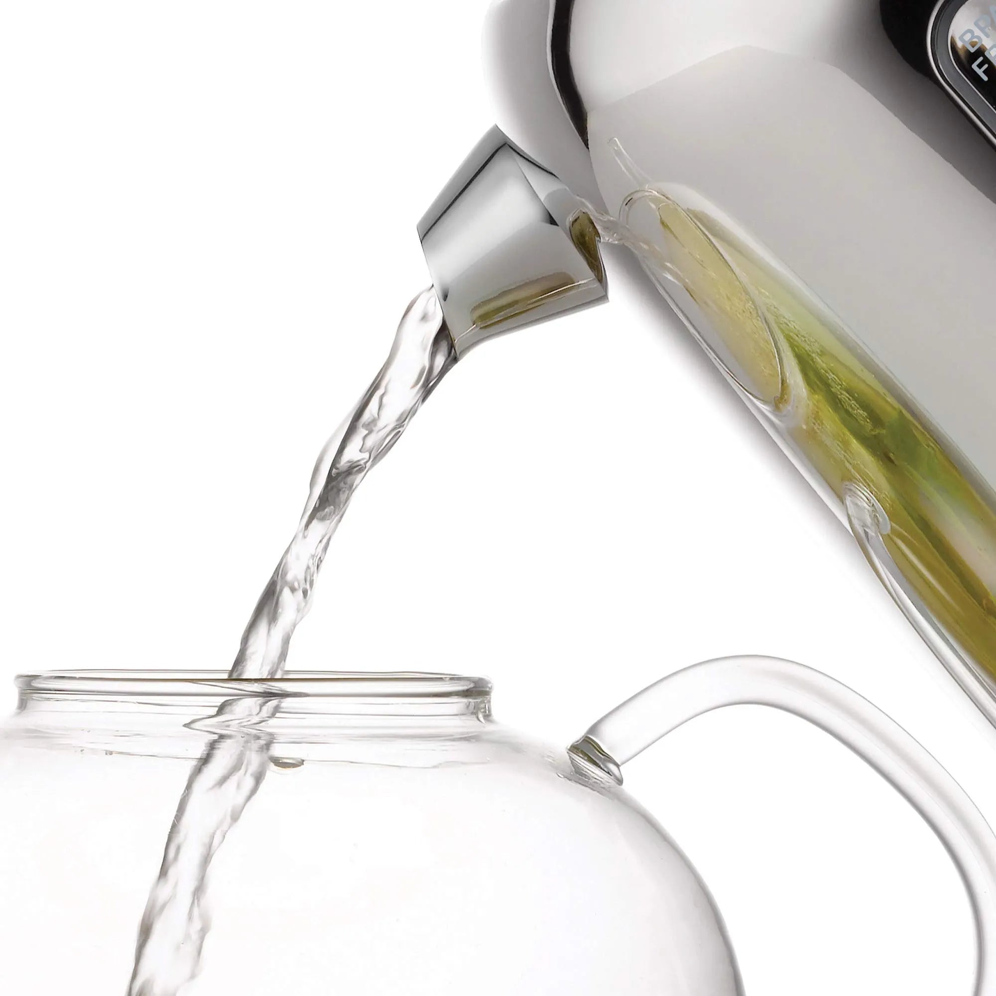 Clear glass carafe being filled with liquid from a white electric kettle on a white background