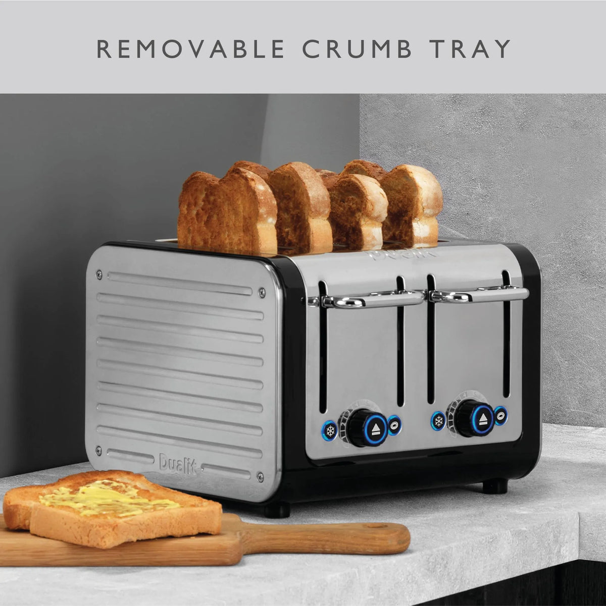 A four-slot toaster with a silver and black body, shown with four slices of toast popping out. A wooden cutting board with toast sits on a light stone countertop in front.