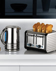 A stainless steel electric kettle and a matching two-slot toaster with four slices of toast, set on a white countertop in a modern kitchen scene.