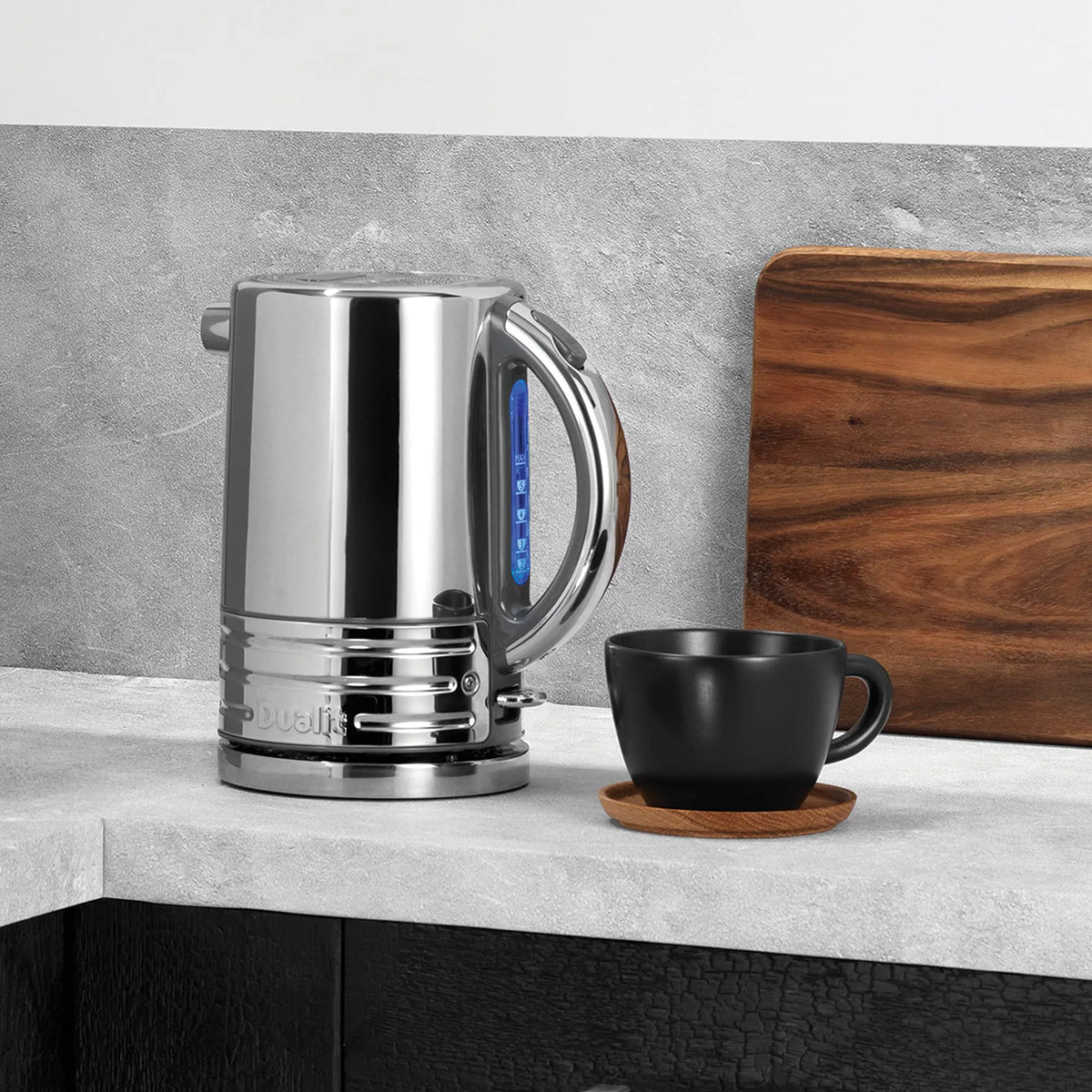 Silver electric kettle on a kitchen counter with a black mug and wooden cutting board.
