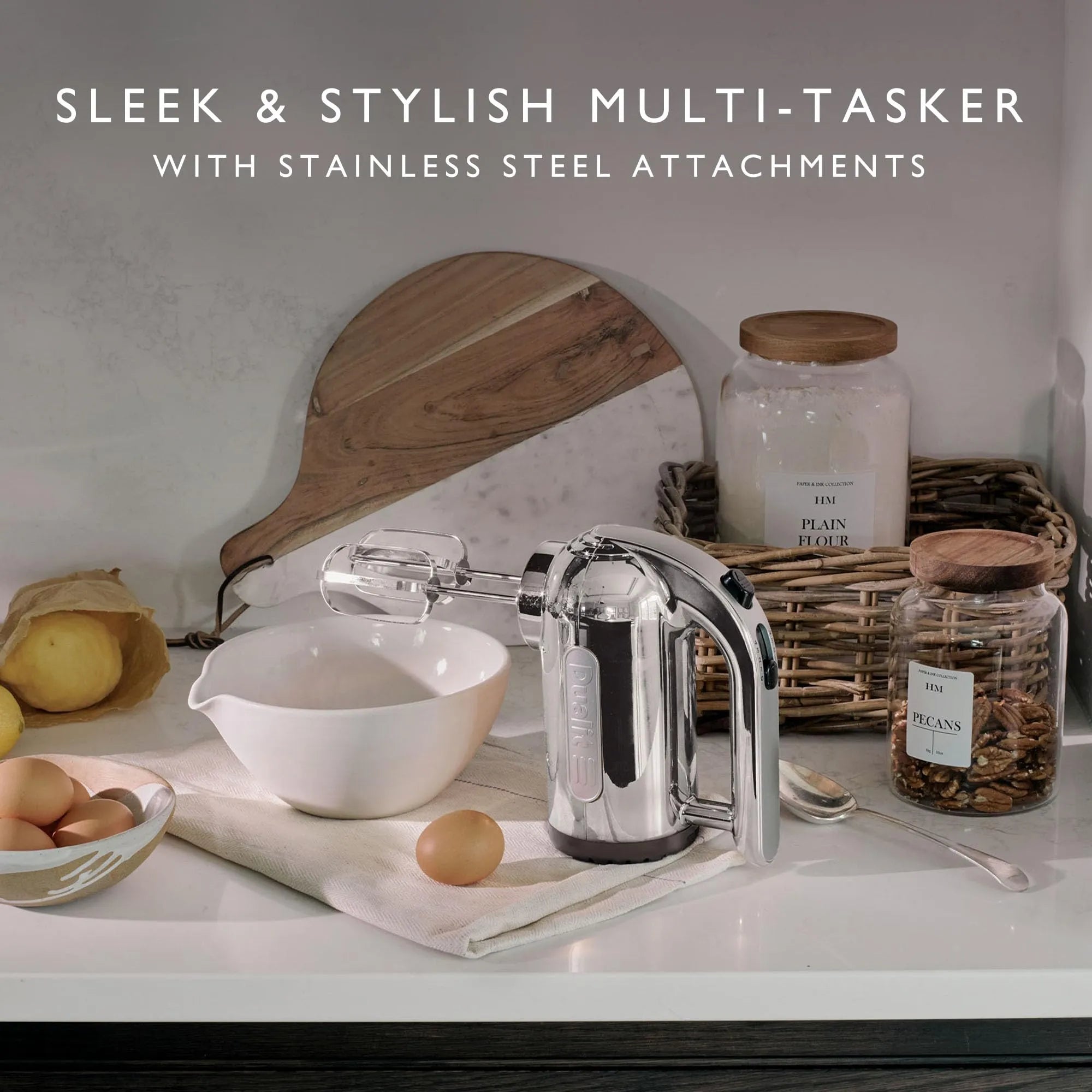 Kitchen scene with a hand mixer on a countertop, surrounded by jars, a cutting board, and eggs.