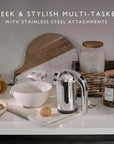 Kitchen scene with a hand mixer on a countertop, surrounded by jars, a cutting board, and eggs.
