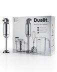 A Dualit hand blender shown next to its retail packaging box on a clean white background. The hand blender has a metallic silver body and black base, and the box displays the product and included accessories like a whisk and measuring cup.