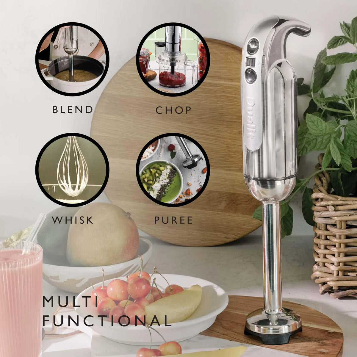 A silver and black immersion blender stands on a wooden board on a kitchen counter, with four circular inset images showing different blending functions: blend, chop, whisk, and puree. The scene includes fruits, a pink drink, and a potted plant in a kitchen setting.