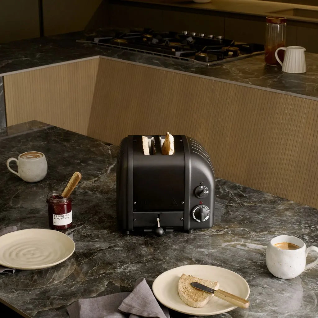 Black toaster on a kitchen counter with toast, mugs, and plates.