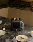 Black toaster on a kitchen counter with toast, mugs, and plates.