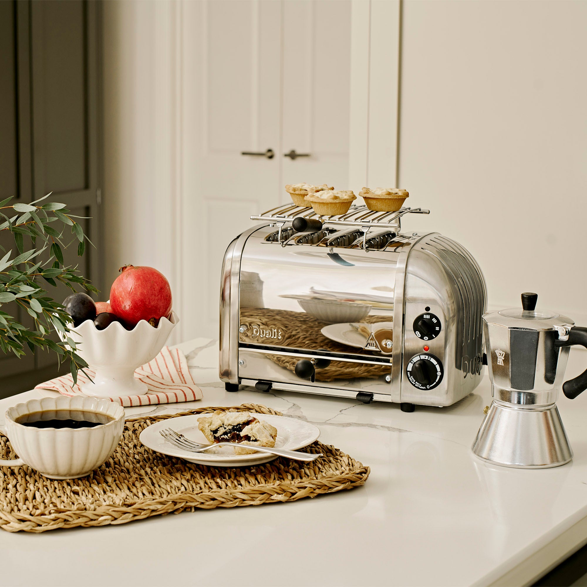 Silver toaster on a kitchen counter with a plate of food, coffee, and a plant.