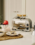 Silver toaster on a kitchen counter with a plate of food, coffee, and a plant.