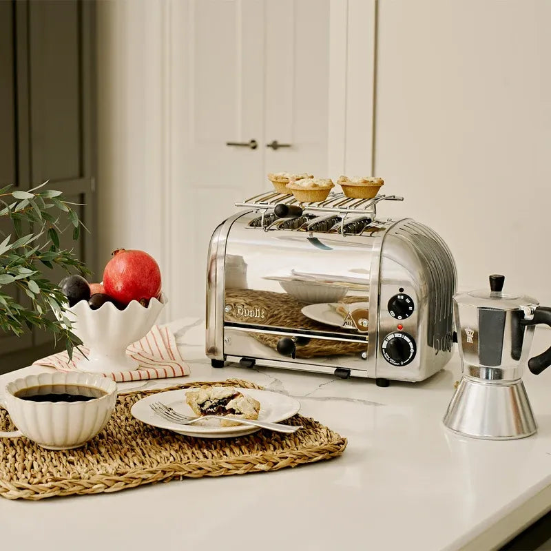 Silver toaster on a kitchen counter with a plate of food, coffee, and a plant.