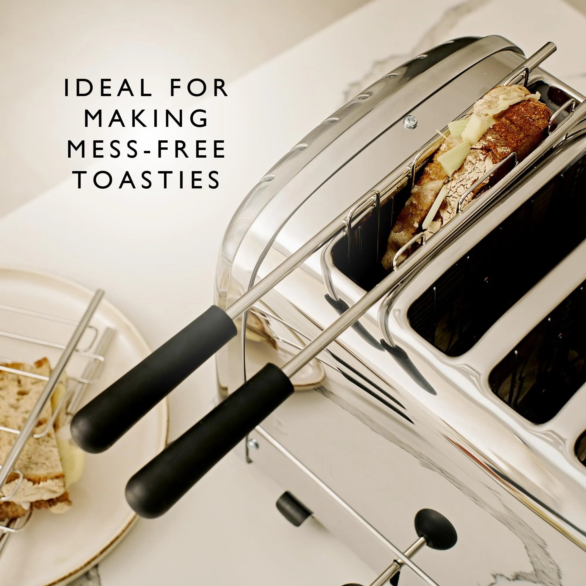 A stainless steel 4-slice toaster with black handles shown on a light countertop, with toast inside one slot and a plate of toast partially visible on the left. Text on the image reads 'IDEAL FOR MAKING MESS-FREE TOASTIES'.