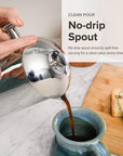 Person using a no-drip spout to pour coffee into a mug with a wooden cutting board and toast in the background.
