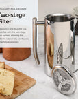 Silver French press coffee maker with a two-stage filter on a marble surface with bread and jars.