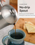 Person pouring coffee from a stainless steel no-drip spout into a blue mug with toast on a wooden board.