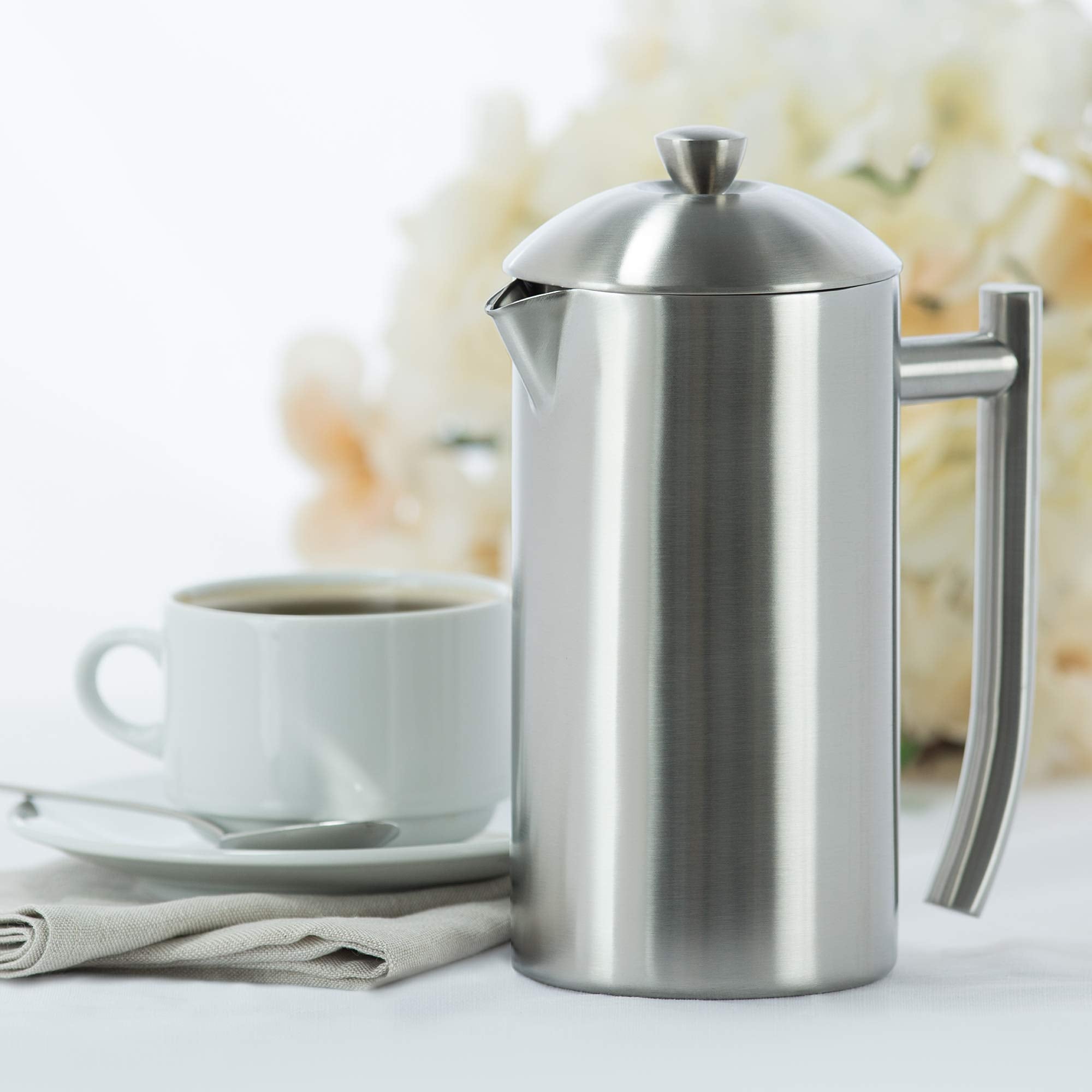 Stainless steel French press and white mug with coffee on a light background