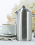 Stainless steel French press and white mug with coffee on a light background