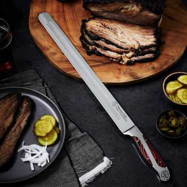 Hammer Stahl Slicer Knife next to sliced pork, pickles, onion, and brown liquid filled glass on a black surface