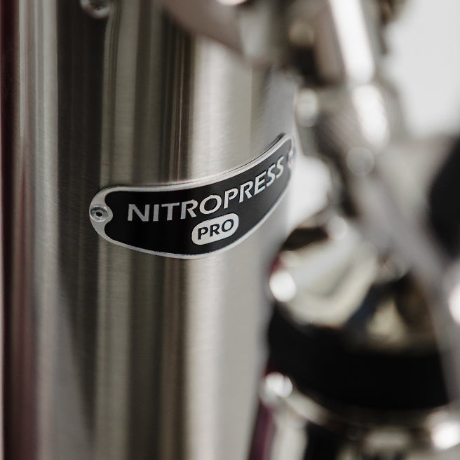 Close-up of a metallic NitroPress Pro coffee machine component with a black oval logo badge.