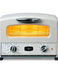 A toaster oven with a white exterior, black feet and handle, and an illuminated orange-yellow heating element visible through the front window. The front panel has two rotary dials, temperature and time settings, and a small orange power indicator light.