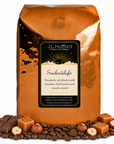 5 lb J.L. Hufford Snickerdelight coffee bag with coffee beans, milk chocolate bar, hazelnuts, and blocks of caramel on a white background