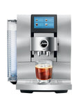 A Jura Z803 commercial-style espresso machine in stainless steel with a digital touch screen, a clear water tank on the left, and a glass of espresso with foam sitting on the drip tray, shown against a plain white background.