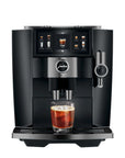 A sleek black and silver Jura coffee machine with a digital touch screen, shown with a glass of iced coffee on its drip tray against a solid white background.