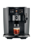 A sleek Jura coffee machine in dark gray and black, shown with a glass of iced coffee on its drip tray against a solid white background.