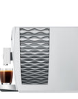 White coffee machine with wavy design next to a glass of coffee on a white background