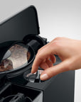 Hand opening a coffee grinder with coffee beans inside, on a light gray background