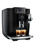 A black Jura E8 coffee machine with a digital display screen, two glass cups of espresso underneath, and a silver steam wand, shown against a solid white background.