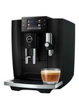A black Jura E8 coffee machine with a digital touch screen, shown with a glass of espresso on its drip tray against a white background.