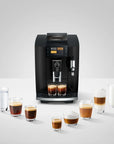 A black Jura coffee machine with two cups of espresso underneath, surrounded by various coffee and milk drinks on a light gray background.