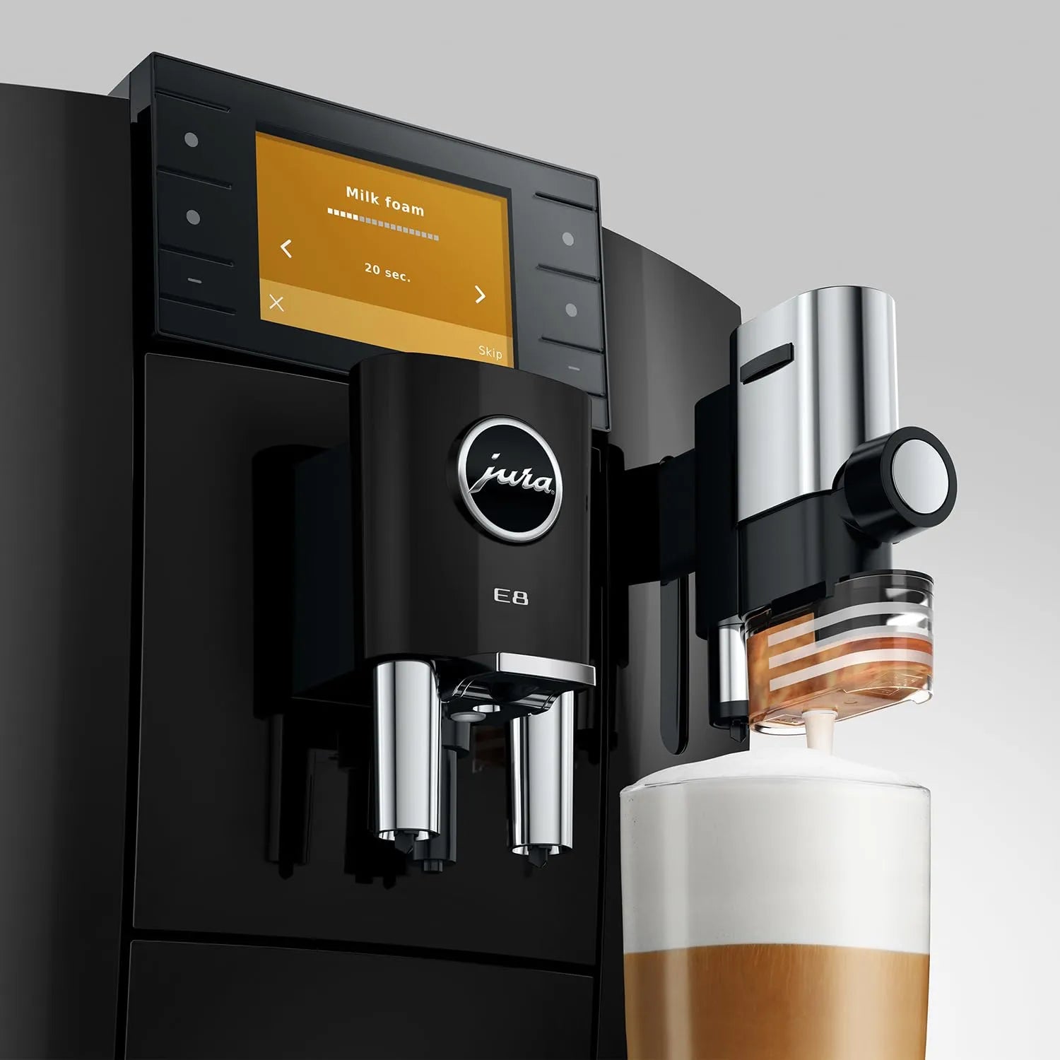 A black Jura E8 automatic coffee machine with a digital display screen, shown dispensing milk foam into a cup of coffee on a light gray background.